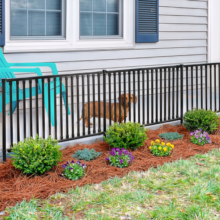 Black metal no-dig fence installed along house with small dog safely enclosed in landscaped yard